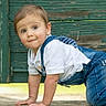 toddler, child, crawling, denim_overalls, white_shirt, outdoor, green_background, wooden_wall, cute, curious, baby, person, portrait, young_child, casual_clothing, hands, knees, face, expression, little_kid