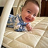 baby, infant, smiling, lying_down, onesie, floral_pattern, quilted_mat, indoor, happy, cute, child, face, hands, head, baby_toy, soft, portrait, person, warm_lighting, home