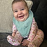 Charli joined the competition — help win amazing prizes! baby, smiling, sitting, bib, onesie, floral_pattern, couch, pillow, happy, infant, indoors, face, child, cute, portrait, cozy, home, soft_lighting, hands, footed_pajamas