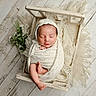 newborn, baby, sleeping, swaddled, knit_wrap, bonnet, wooden_crate, flowers, rustic, wooden_floor, cozy, peaceful, infant, portrait, soft_texture, cream_color, cute, resting, wrapped, adorable