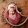 newborn, baby, sleeping, wrapped, hat, pink, purple, wooden_bowl, wooden_floor, cozy, soft_texture, cute, peaceful, infant, portrait, indoors, resting, child, headwear, blanket