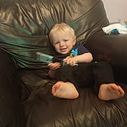 Richie joined the competition — help win amazing prizes! toddler, child, toy, leather_chair, barefoot, smile, indoor, casual, young_child, furniture, relaxed, couch, playful, blurry, happy, person, home, clothing, short_sleeve, pants