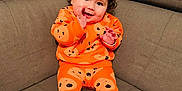 Aliénor participe au concours pour gagner de l'argent avec cette photo : baby, child, comfort, couch, curly_hair, cute, face, footwearless, hands, happy, home, indoor, infant, orange_clothing, pajamas, playful, plush_toy, sitting, smile, window