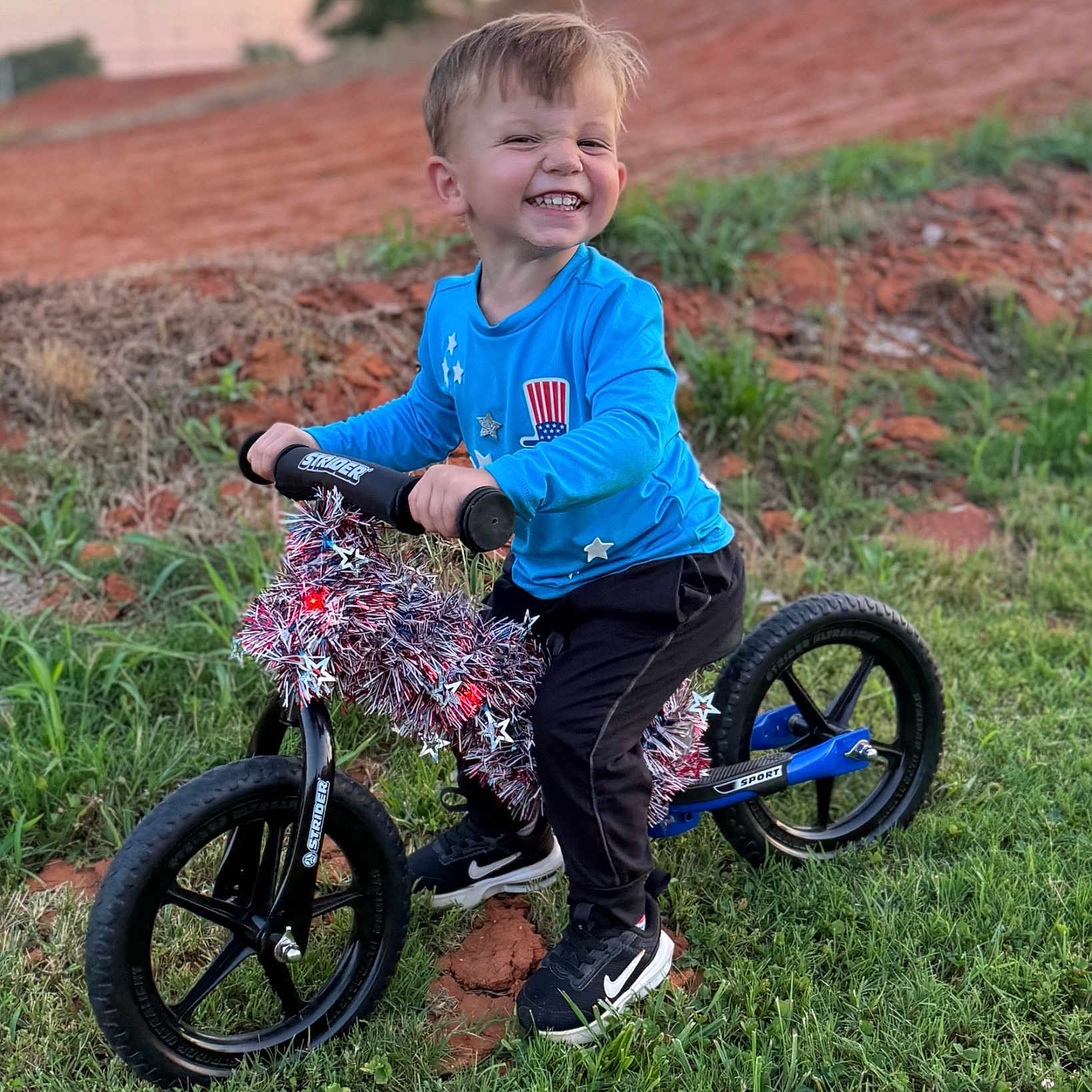 Houston Lane joined the competition — help win amazing prizes! balance_bike, black_pants, black_shoes, blue_shirt, child, dirt, fun, grass, happy, nature, nike, outdoor, playing, portrait, smiling, stars, sunset, tinsel, toy, young_boy