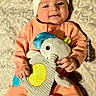 baby, infant, child, portrait, smiling, happy, headband, bow, peach_outfit, onesie, stuffed_animal, elephant_toy, toy, blanket, lying_down, indoor, nursery, patterned_background, close_up, photography