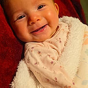 Julietta is registered to the contest to win money with this photo: baby, infant, child, smiling, portrait, close_up, face, eyes, fluffy_blanket, red_blanket, floral_clothing, pink_outfit, lying_down, cozy, indoors, soft_texture, warm_lighting, happy, photograph, adorable