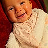 baby, infant, child, smiling, portrait, close_up, face, eyes, fluffy_blanket, red_blanket, floral_clothing, pink_outfit, lying_down, cozy, indoors, soft_texture, warm_lighting, happy, photograph, adorable