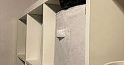 Peaches is registered to the contest to win money with this photo: cat, black_cat, storage_bin, shelf, furniture, indoor, minimalist, white, peeking, hidden, pet, cozy, animal, home, container, cubicle, quiet, resting, cautious, curious