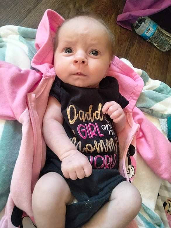 Emma is registered to the contest to win money with this photo: arm, baby, baby_carriage, baby_toddler_clothing, cheek, clothing, comfort, dress, eyelash, face, finger, hand, head, human_body, iris, lip, person, pink, product, skin