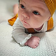 Allison is registered to the contest to win money with this photo: baby, infant, face, hat, yellow_hat, white_blanket, knitted_blanket, close_up, cute, child, skin, sleeve, hand, fist, lying_down, portrait, indoor, soft_light, expression, young
