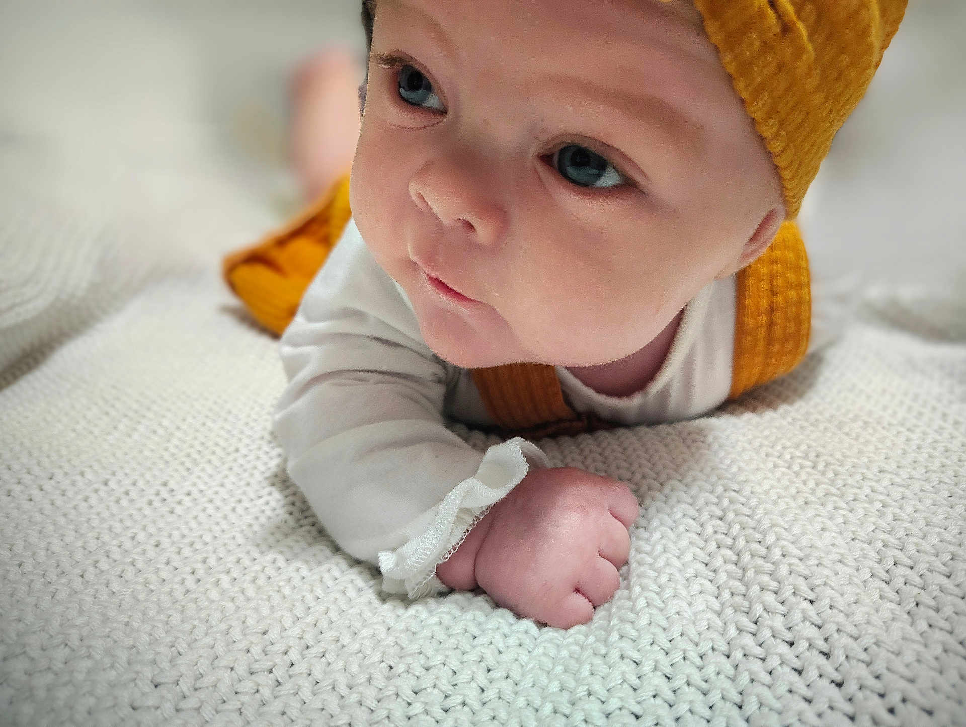 Allison is registered to the contest to win money with this photo: baby, infant, face, hat, yellow_hat, white_blanket, knitted_blanket, close_up, cute, child, skin, sleeve, hand, fist, lying_down, portrait, indoor, soft_light, expression, young