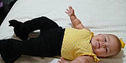 Allison is registered to the contest to win money with this photo: baby, bed, black_pants, child, chubby_arms, clothing, cute, face, happy, head, indoor, infant, lying_down, person, portrait, reaching_out, smile, white_bedspread, yellow_top, young_child