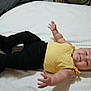 baby, bed, black_pants, child, chubby_arms, clothing, cute, face, happy, head, indoor, infant, lying_down, person, portrait, reaching_out, smile, white_bedspread, yellow_top, young_child