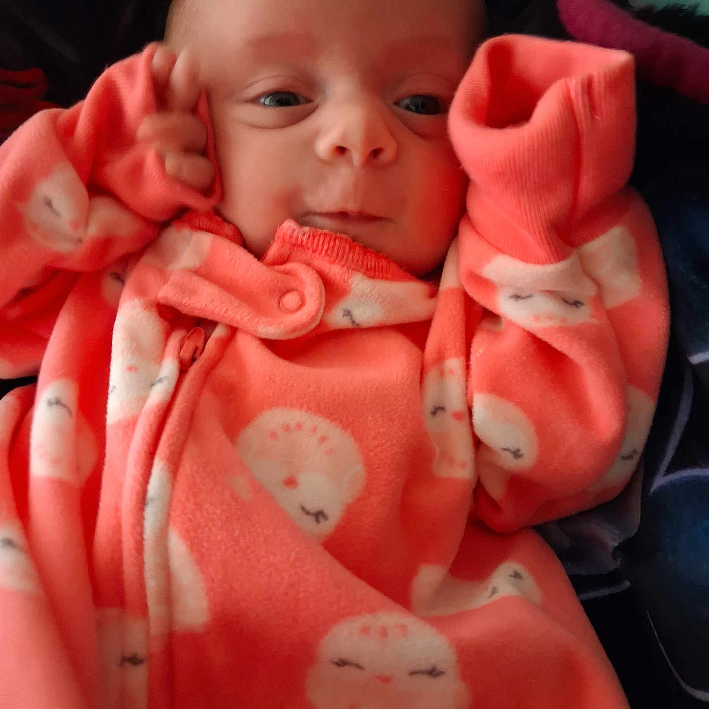Aurora is registered to the contest to win money with this photo: baby, infant, onesie, orange_clothing, sleepy_moon_pattern, hands_near_face, curious_expression, portrait, closeup, cozy, cute, child, newborn, soft_fabric, indoor, warm, small_hands, head, face, eyes