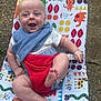 animal_prints, baby, bib, blue_eyes, child, colorful_chair, cute, feet, happy, infant, joyful, legs, outdoor, pattern, playful, portrait, red_harness, seat, smiling, sunlight
