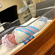 Brianna is registered to the contest to win money with this photo: newborn, baby, swaddled, hospital, bassinet, blanket, hat, pink, bow, sleeping, face, infant, wood, medical, room, furniture, patient, cute, child, healthcare