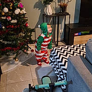 Cally participe au concours pour gagner de l'argent avec cette photo : toddler, child, christmas_tree, holiday, festive_clothing, living_room, toy_bike, blanket, couch, floor_tiles, vase, flowers, decor, smile, hooded_onesie, indoor, furniture, shadow, present, happy