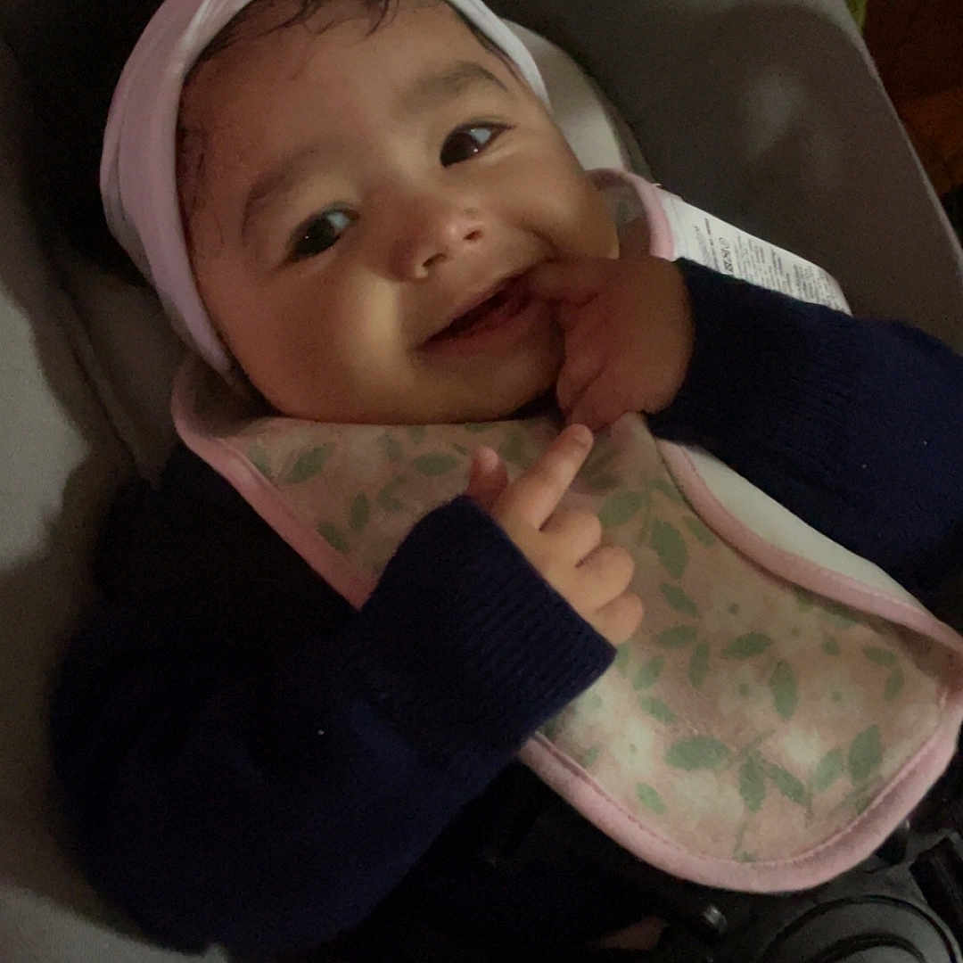 Inaya a rejoint le concours — aidez-le/la à gagner de superbes lots ! baby, smiling, headband, flower, bib, cushion, seat, clothing, hand, finger, face, person, infant, cute, indoors, portrait, happy, child, young, cozy