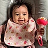 baby, infant, smiling, pink_bib, strawberry_pattern, rattle, cushioned_seat, happy, child, cute, portrait, baby_clothes, toy, indoor, young_child, person, seat_belt, head, hand, expressive_face