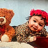 baby, teddy_bear, flower_crown, leopard_print, plush, red_bow, soft_toy, child, portrait, cute, smile, indoor, cushion, furniture, happy, headband, infant, toy, cozy, baby_clothing