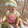 baby, child, infant, pink_overalls, white_headband, bow, socks, pink_blanket, wooden_sign, ten_months, cute, sitting, indoor, soft_texture, floral_pattern, person, toddler, clothing, baby_girl, portrait