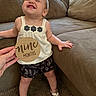 baby, child, smile, happy, couch, indoor, carpet, clothing, footwear, person, wooden_sign, hand, shorts, top, sandal, face, skin, furniture, home, infant