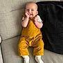Myla joined the competition — help win amazing prizes! baby, child, smiling, yellow_overalls, white_socks, couch, pillow, indoor, portrait, happy, infant, clothing, person, seated, cute, playful, furniture, home, comfortable, young_child
