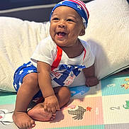 Nehemiah joined the competition — help win amazing prizes! baby, child, smiling, sitting, play_mat, colorful, patriotic_clothing, stars, stripes, headwear, happy, indoors, foot, hand, person, infant, cushion, clothing, cute, portrait