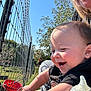Ripp is registered to the contest to win money with this photo: arm, baby, black_shirt, bottle, child, closeup, face, feeding_bottle, fence, grass, happy, nature, outdoor, person, playful, red_bucket, smiling, sunlight, tree, wire_fence