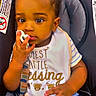 baby, child, infant, car_seat, seated, portrait, curious, toy, bib, striped_shirt, blue_pants, brown_hair, dark_skin, large_eyes, indoor, vehicle, safety_seat, hands, colorful_clothing, close_up