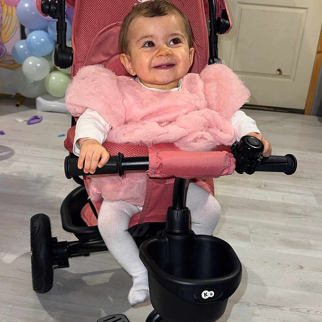 Mia participe au concours pour gagner de l'argent avec cette photo : baby, balloons, child, cute, door, floor, handlebars, happy, indoor, pedals, pink_dress, play, seat, smile, tiara, toddler, toy, tricycle, wheel, white_tights