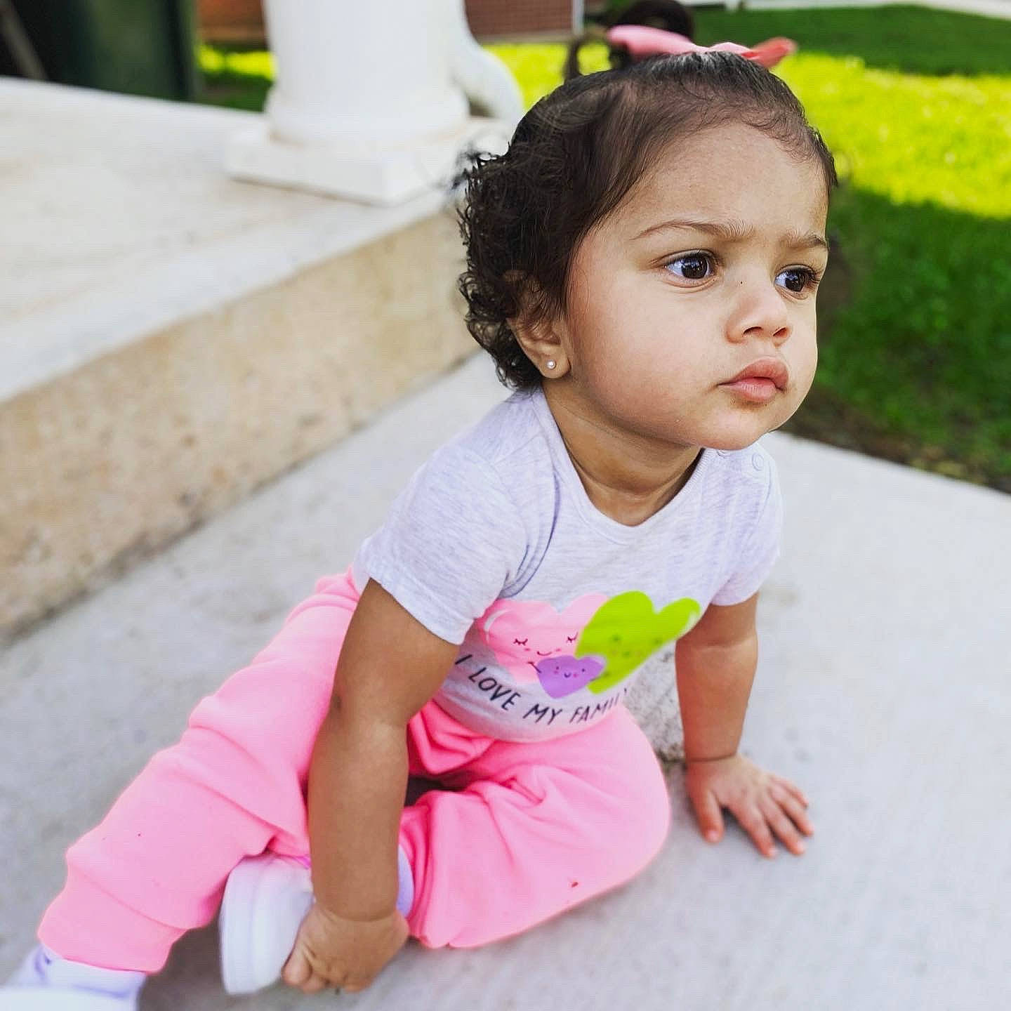 Essence is registered to the contest to win money with this photo: baby, baby_toddler_clothing, black_hair, cheek, face, grass, green, hair, happy, head, leisure, neck, person, pink, shoulder, skin, sleeve, smile, standing, thigh