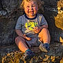 toddler, child, smiling, curly_hair, outdoor, rock, stone_steps, casual_clothing, shorts, tshirt, footwear, sunlight, happy, sitting, portrait, cute, young, playful, nature, daylight