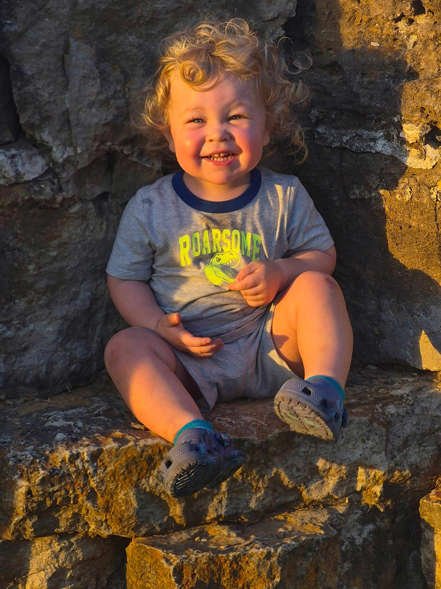 Nixon joined the competition — help win amazing prizes! toddler, child, smiling, curly_hair, outdoor, rock, stone_steps, casual_clothing, shorts, tshirt, footwear, sunlight, happy, sitting, portrait, cute, young, playful, nature, daylight