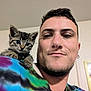 man, cat, kitten, shoulder, selfie, indoor, tie_dye_shirt, tabby, young_adult, facial_hair, earring, smile, pet, animal, cute, curious, portrait, casual, friendship, home