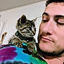 Fluke Ellington is registered to the contest to win money with this photo: man, kitten, cat, pet, tie_dye_shirt, shoulder, indoor, young_adult, facial_hair, curious, close_up, affection, animal, domestic_animal, portrait, feline, cute, companion, looking_at_each_other, soft_background