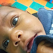 True joined the competition — help win amazing prizes! baby, child, infant, close_up, portrait, face, eyes, curious, indoor, play_mat, colorful, floor, blue_clothing, sleeve, lying_down, looking_at_camera, skin, photography, home, play_area