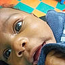 baby, child, infant, close_up, portrait, face, eyes, curious, indoor, play_mat, colorful, floor, blue_clothing, sleeve, lying_down, looking_at_camera, skin, photography, home, play_area