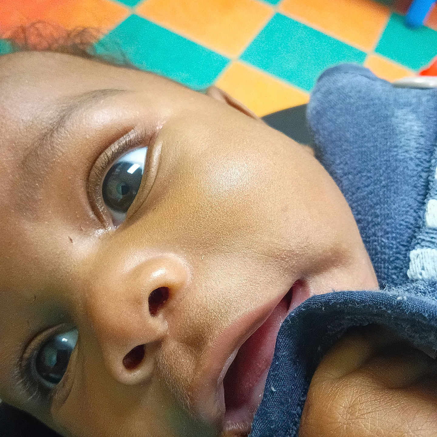 True joined the competition — help win amazing prizes! baby, child, infant, close_up, portrait, face, eyes, curious, indoor, play_mat, colorful, floor, blue_clothing, sleeve, lying_down, looking_at_camera, skin, photography, home, play_area