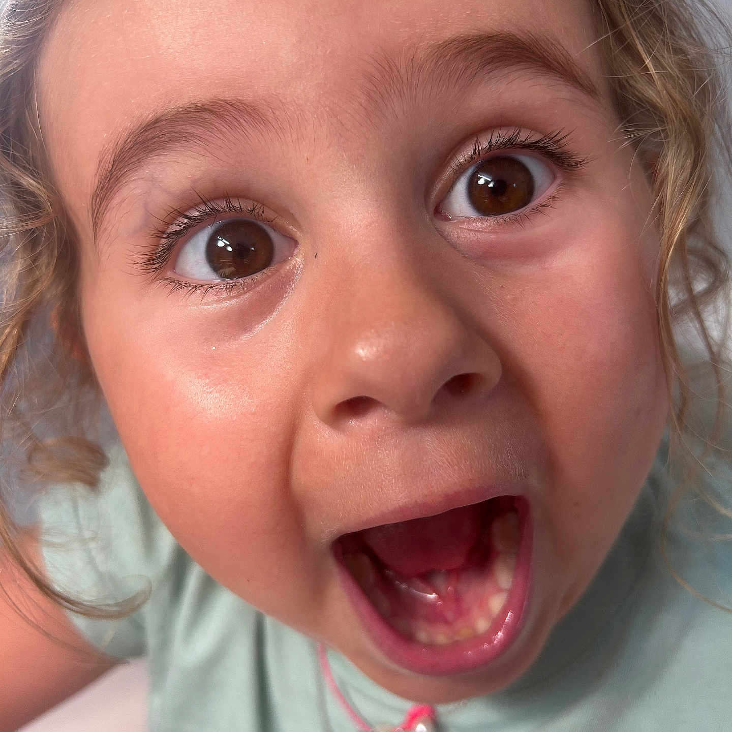 Inaya a rejoint le concours — aidez-le/la à gagner de superbes lots ! brown_eyes, child, childhood, close_up, curly_hair, cute, emotion, expression, eyelashes, face, happy, indoors, light_green_shirt, mouth_open, necklace, person, portrait, skin, surprised, young