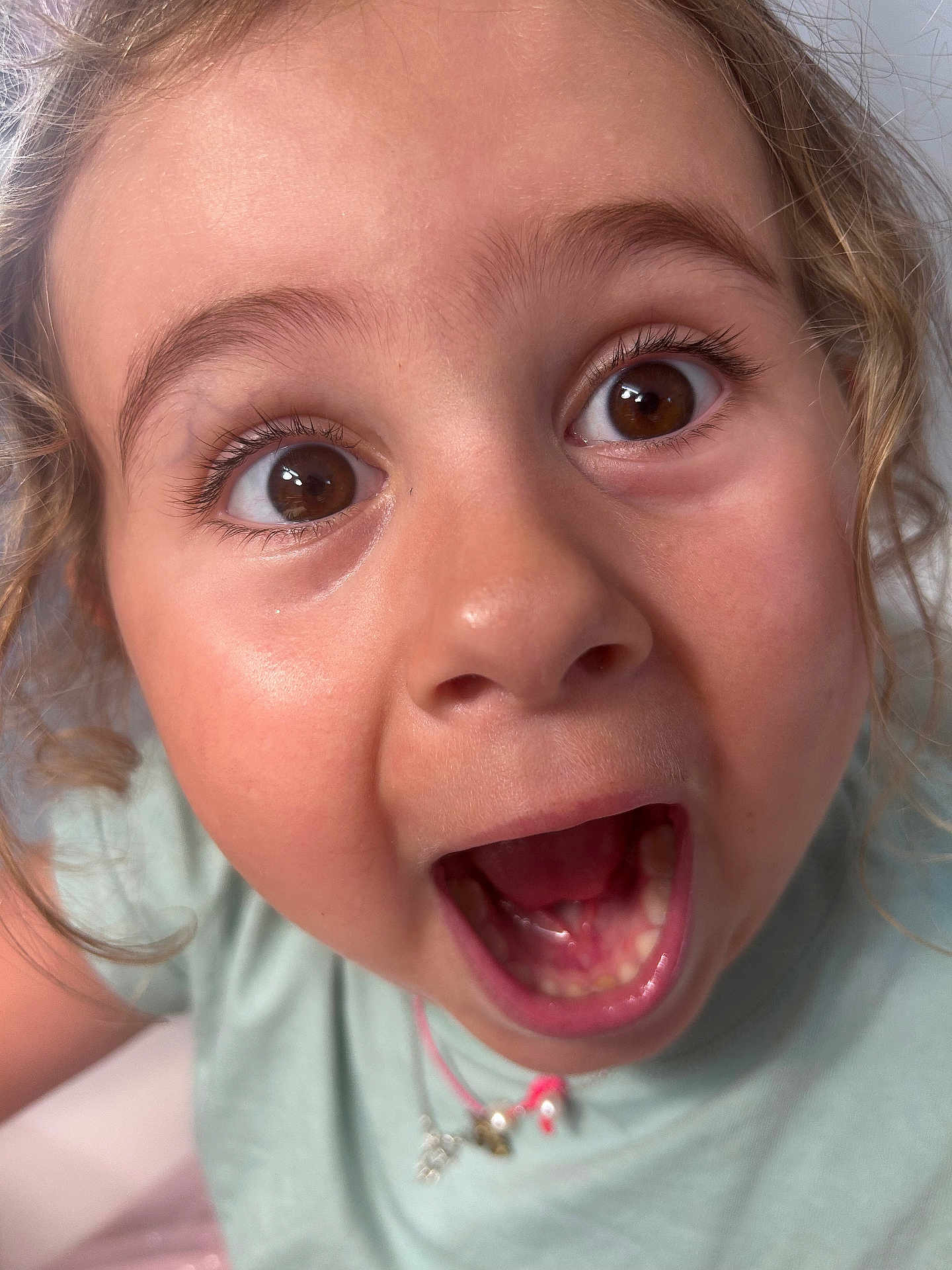 Inaya a rejoint le concours — aidez-le/la à gagner de superbes lots ! child, face, close_up, curly_hair, surprised, mouth_open, brown_eyes, necklace, light_green_shirt, expression, portrait, cute, person, young, indoors, skin, eyelashes, emotion, childhood, happy