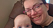 Elizabeth joined the competition — help win amazing prizes! adult, baby, candid, chair, closeup, face, family, glasses, happy, head, home, indoor, orange_onesie, person, portrait, relaxing, skin, smile, striped_clothing, window