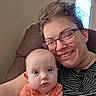 Elizabeth joined the competition — help win amazing prizes! adult, baby, glasses, smile, face, portrait, indoor, window, chair, striped_clothing, orange_onesie, skin, person, happy, family, closeup, head, candid, relaxing, home
