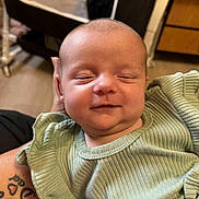 Oaklynn is registered to the contest to win money with this photo: baby, infant, smile, green_clothing, ribbed_fabric, tattoo, arm, indoor, furniture, crib, person, face, closeup, happy, child, newborn, skin, head, soft_light, portrait