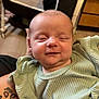 baby, infant, smile, green_clothing, ribbed_fabric, tattoo, arm, indoor, furniture, crib, person, face, closeup, happy, child, newborn, skin, head, soft_light, portrait