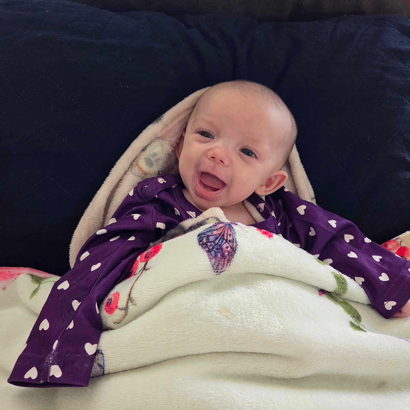 Piper joined the competition — help win amazing prizes! baby, blanket, couch, cozy, cute, eyes, face, happy, heart_pattern, indoors, infant, mouth, newborn, pillow, portrait, purple_clothing, smiling, soft_texture, tongue, wrapped