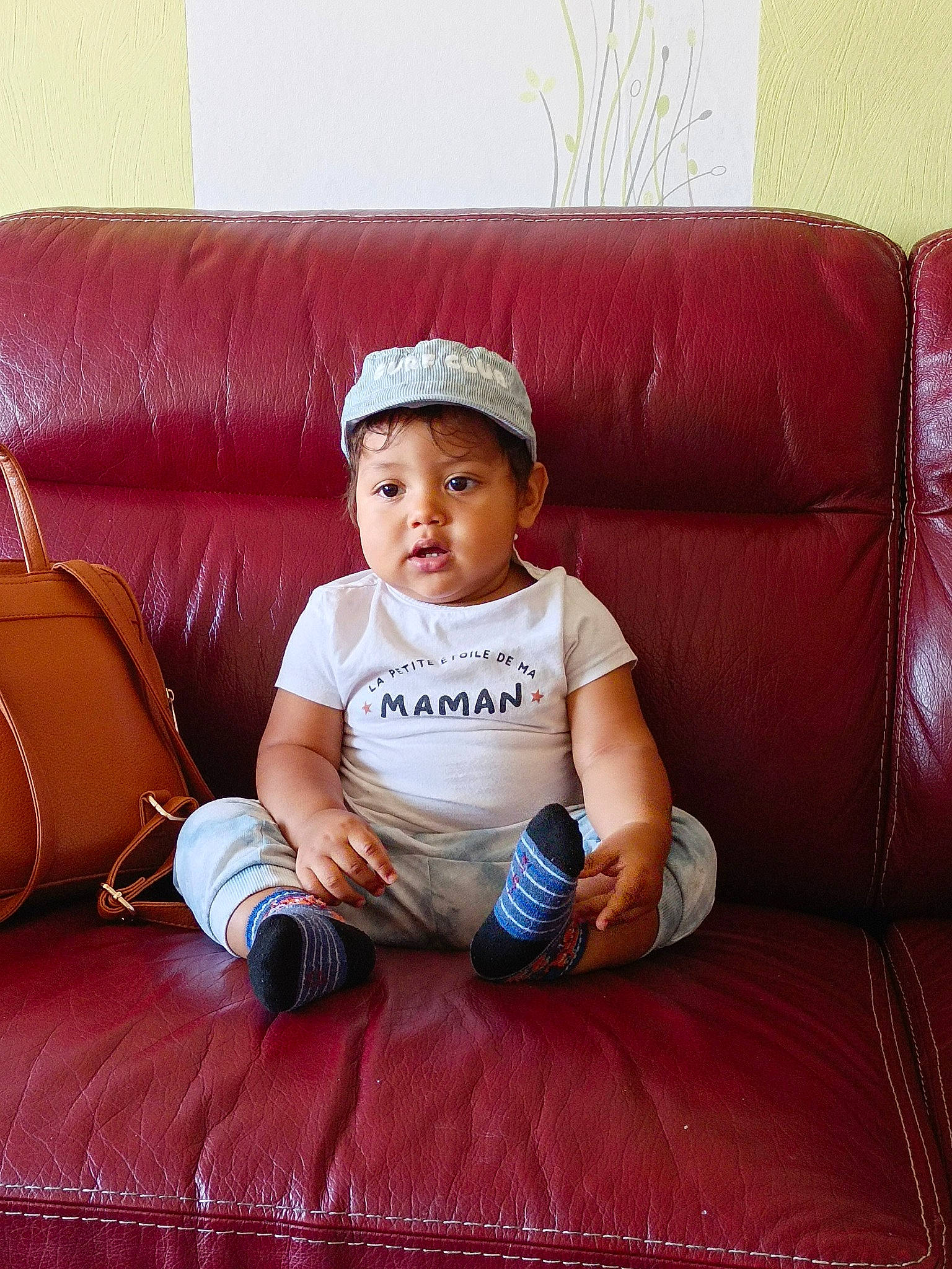 Matis a rejoint le concours — aidez-le/la à gagner de superbes lots ! baby, baby_toddler_clothing, cap, child, comfort, couch, face, flash_photography, flooring, human_leg, knee, leisure, living_room, person, room, sitting, studio_couch, t_shirt, throw_pillow, toddler