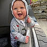 baby, child, hoodie, smiling, blue_eyes, car_trunk, outdoor, stone_wall, grass, sunset, cute, clothing, happy, person, infant, casual, daylight, vehicle, playing, expression