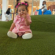 Maria Catalina is registered to the contest to win money with this photo: baby, child, toddler, girl, pink_dress, hair_bows, snack, grass, indoor, play_area, toy_horse, smiling, shop_window, mannequins, people, seated, happy, casual_clothing, retail_store, green