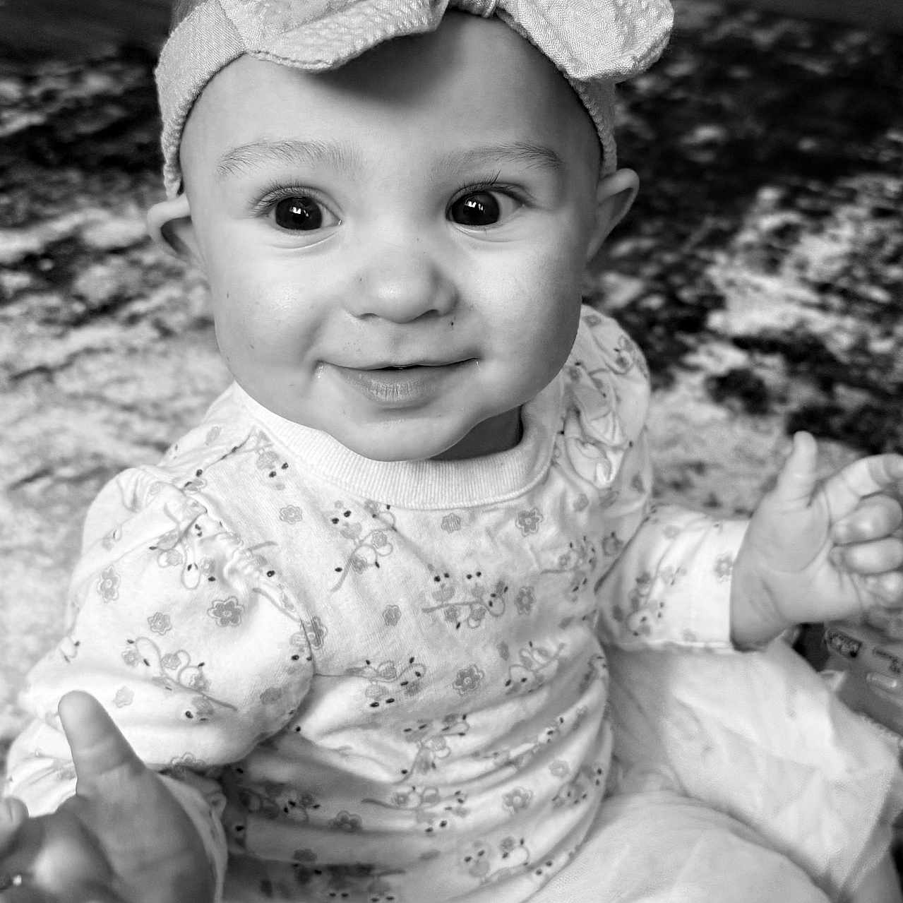 Stella is registered to the contest to win money with this photo: baby, child, headband, bow, smile, face, hand, clothing, long_sleeve, dress, indoor, carpet, floor, cute, portrait, sitting, toddler, person, happy, black_and_white